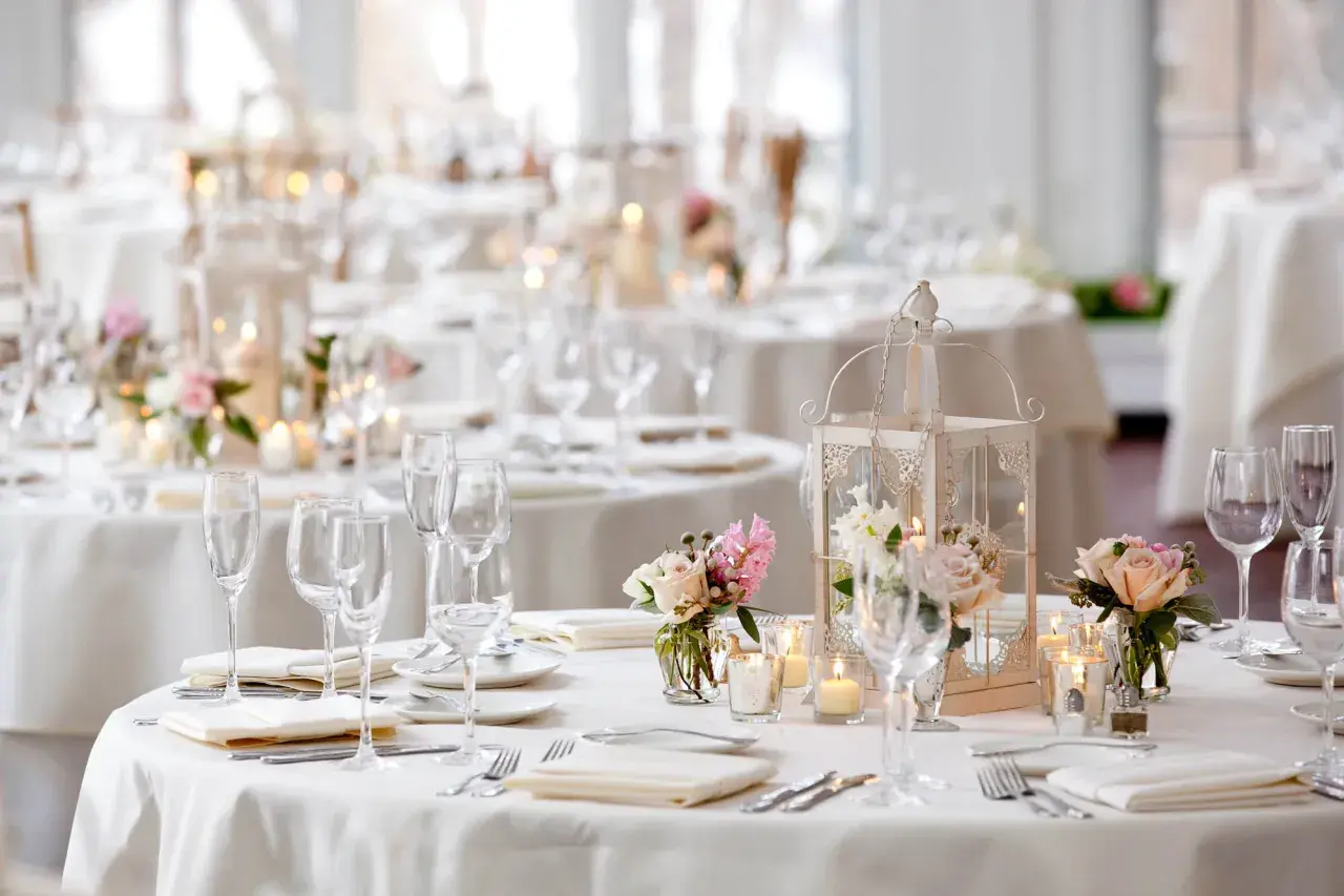 Disposition table mariage élégante avec lanternes, bougies et bouquets de roses. Verres à pied et couverts prêts pour les invités.