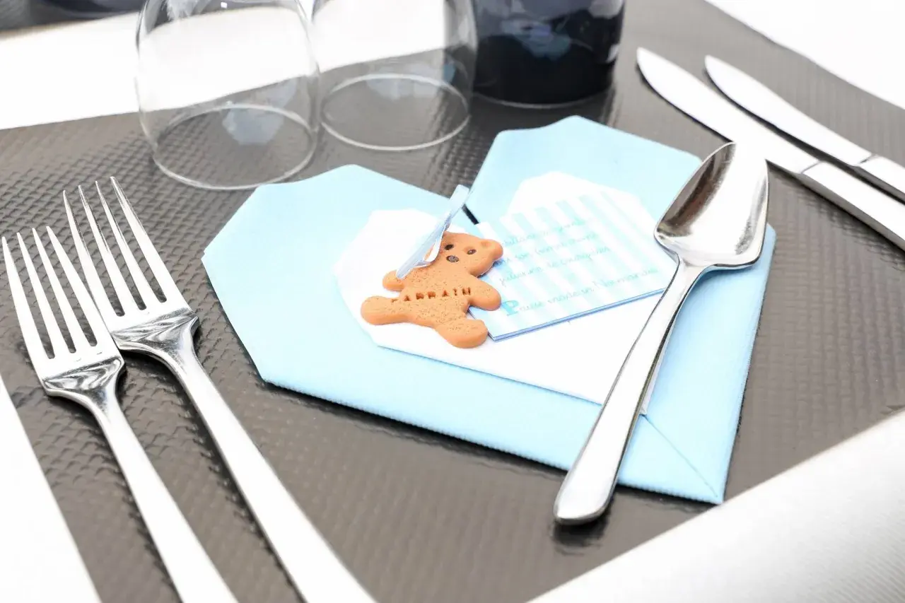 Un biscuit en forme d'ours sur une serviette bleue, prêt pour un baptême. Le tableau budget baptême est bien organisé.