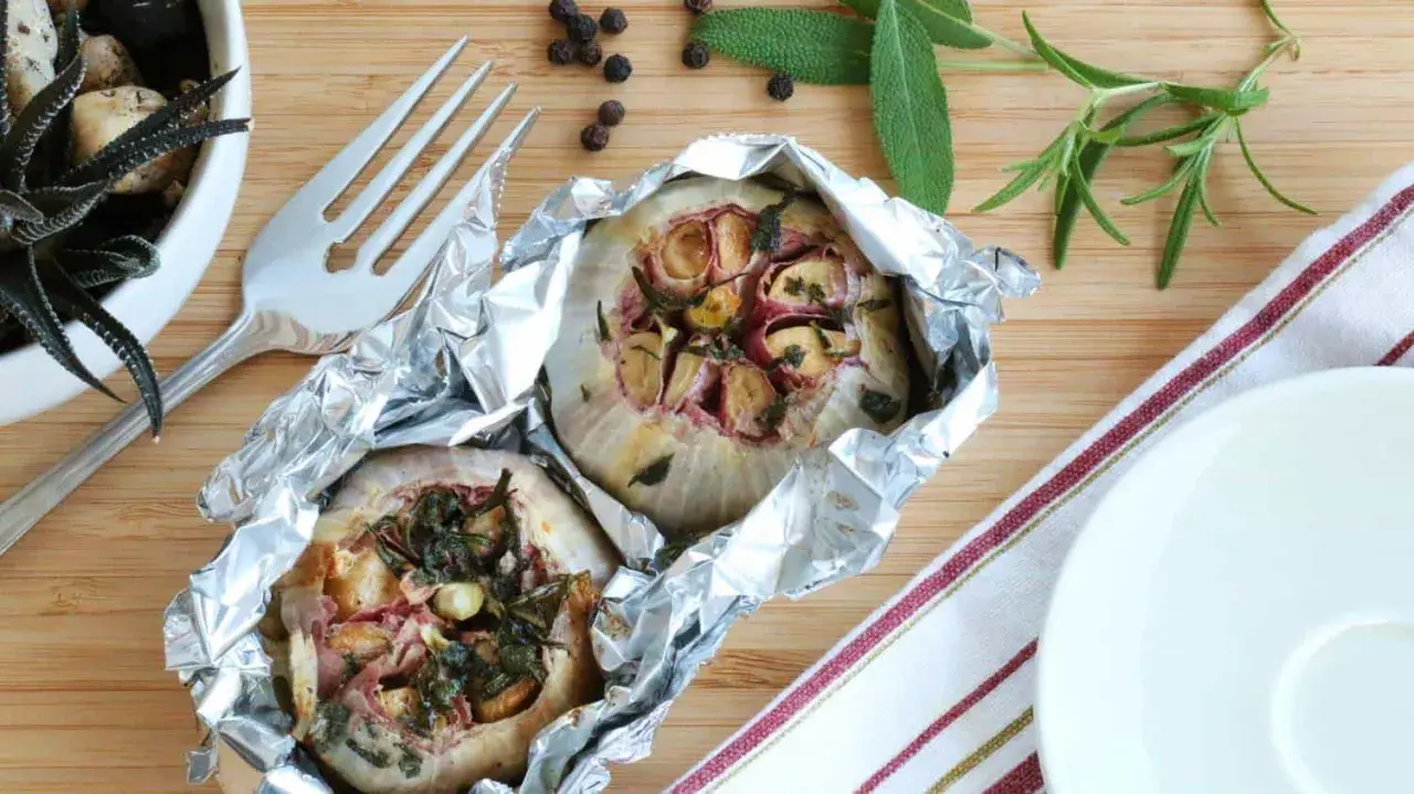 Deux têtes d'ail au barbecue, enveloppées dans du papier d'aluminium, avec des herbes et des épices.