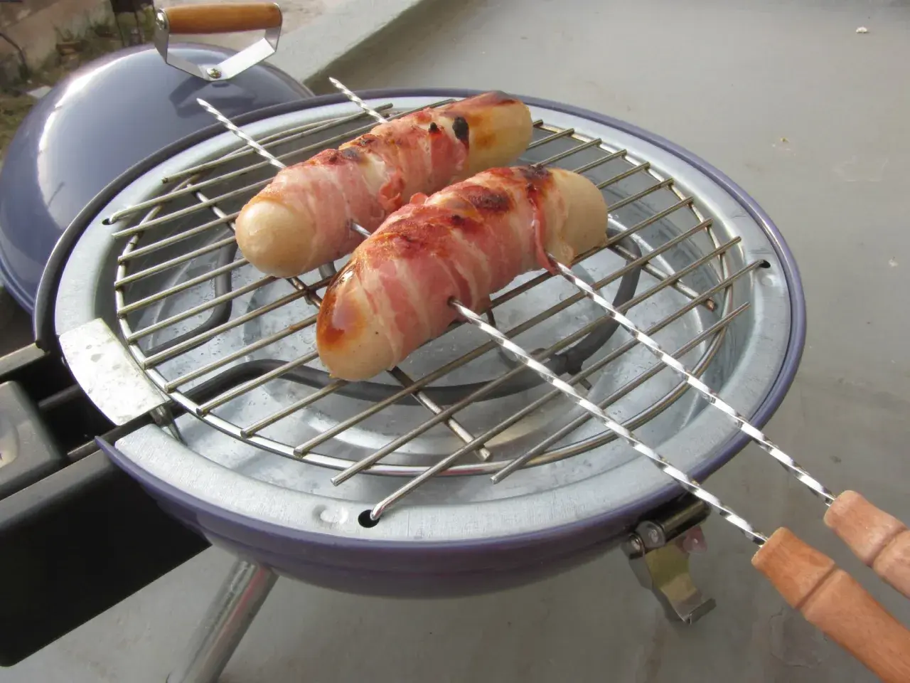 Deux boudins blancs enroulés de lard grillent sur un barbecue. Un délice pour un barbecue estival.