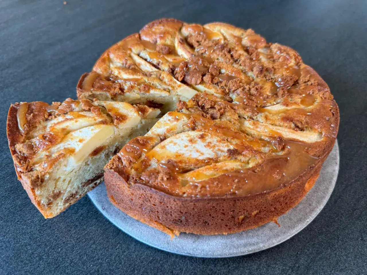 Gâteau pomme spéculoos, une part coupée révèle la texture moelleuse et les morceaux de spéculoos. Un délice gourmand.