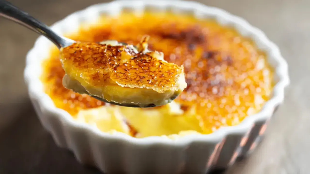 Une cuillère soulève une bouchée de crème brûlée clementine, révélant sa croûte caramélisée craquante et sa crème onctueuse.