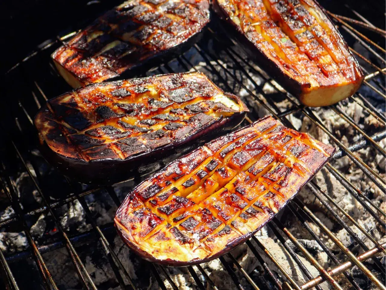 Aubergines coupées en deux, grillées au barbecue, avec des marques de cuisson caramélisées et une chair tendre.