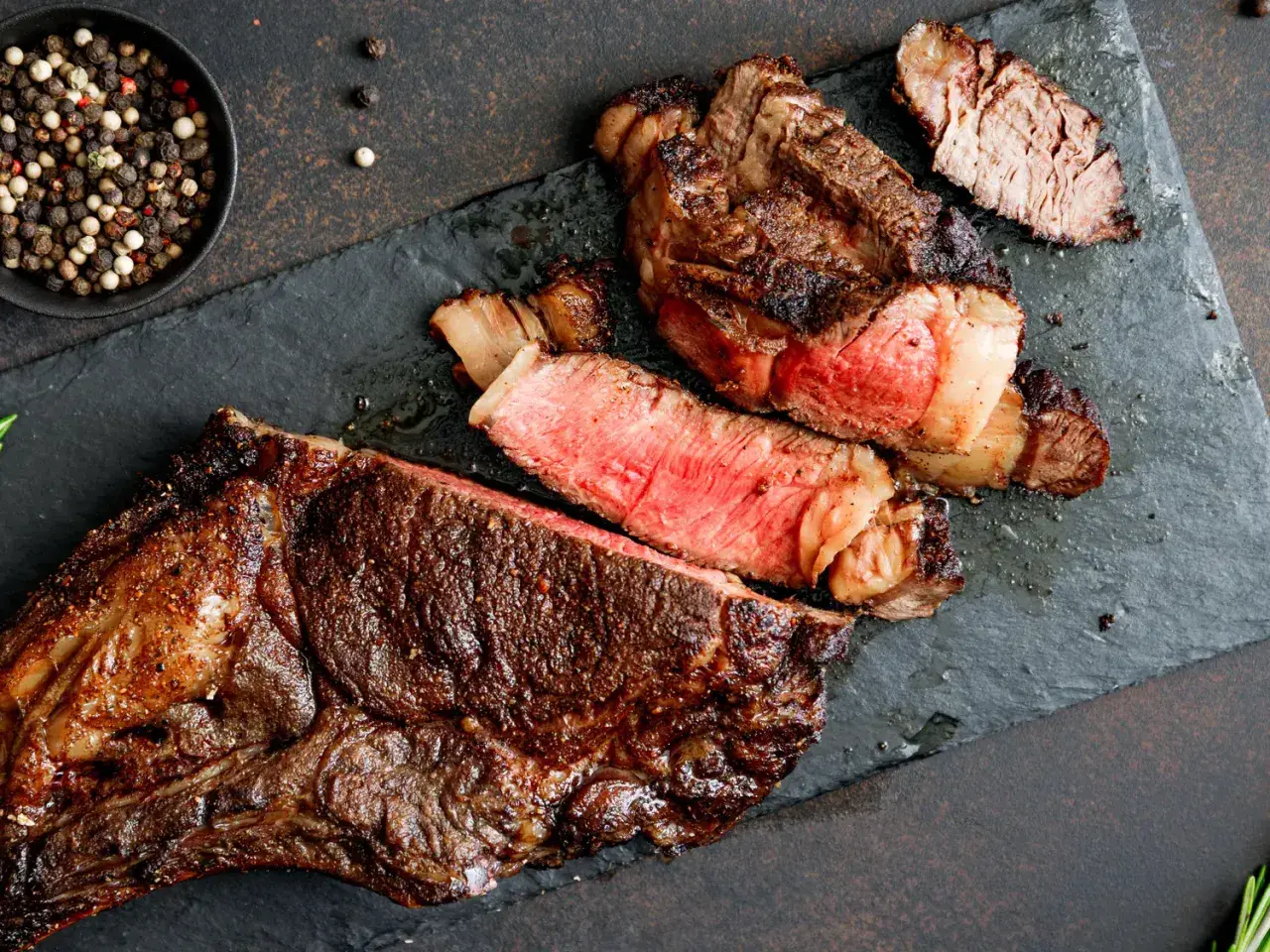 Un steak de bœuf juteux, coupé en tranches, révèle une cuisson parfaite grâce à la méthode de cuisson reverse sear. Poivre noir et blanc en accompagnement.