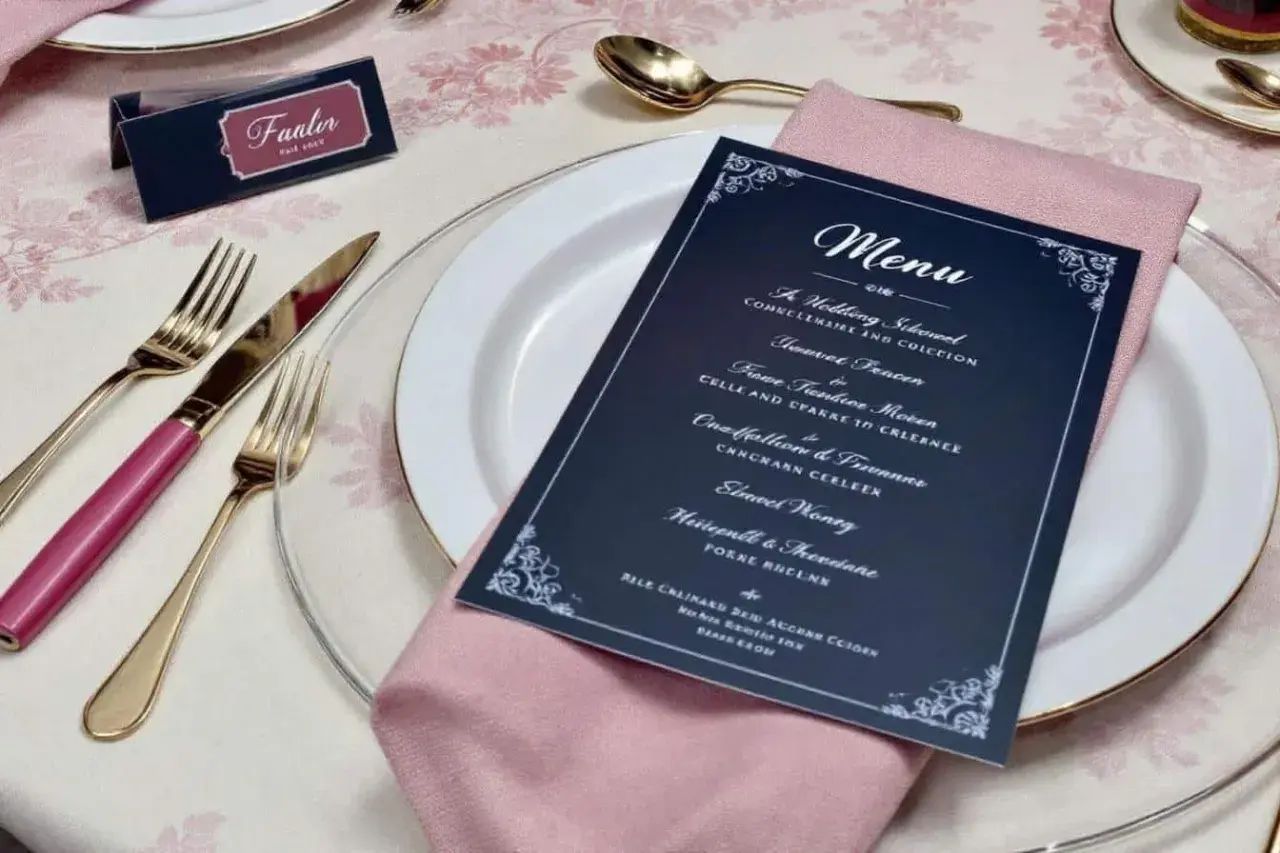 Une table dressée pour un mariage, avec une carte de menu originale, des couverts dorés et une serviette rose.