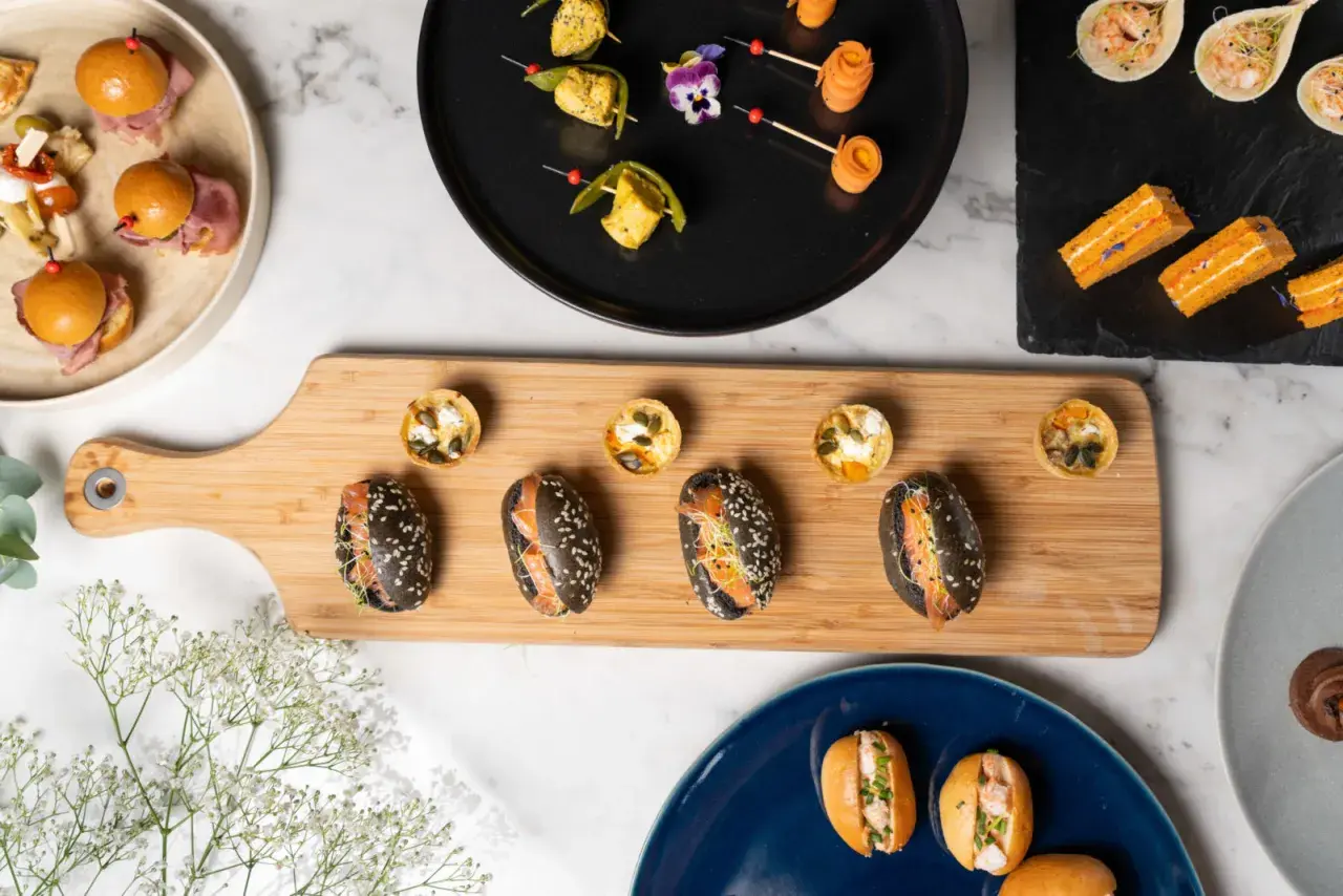 Assortiment de bouchées variées, parfaites pour un manger froid. Mini-burgers, tartes salées et sandwichs au saumon sur planche en bois.
