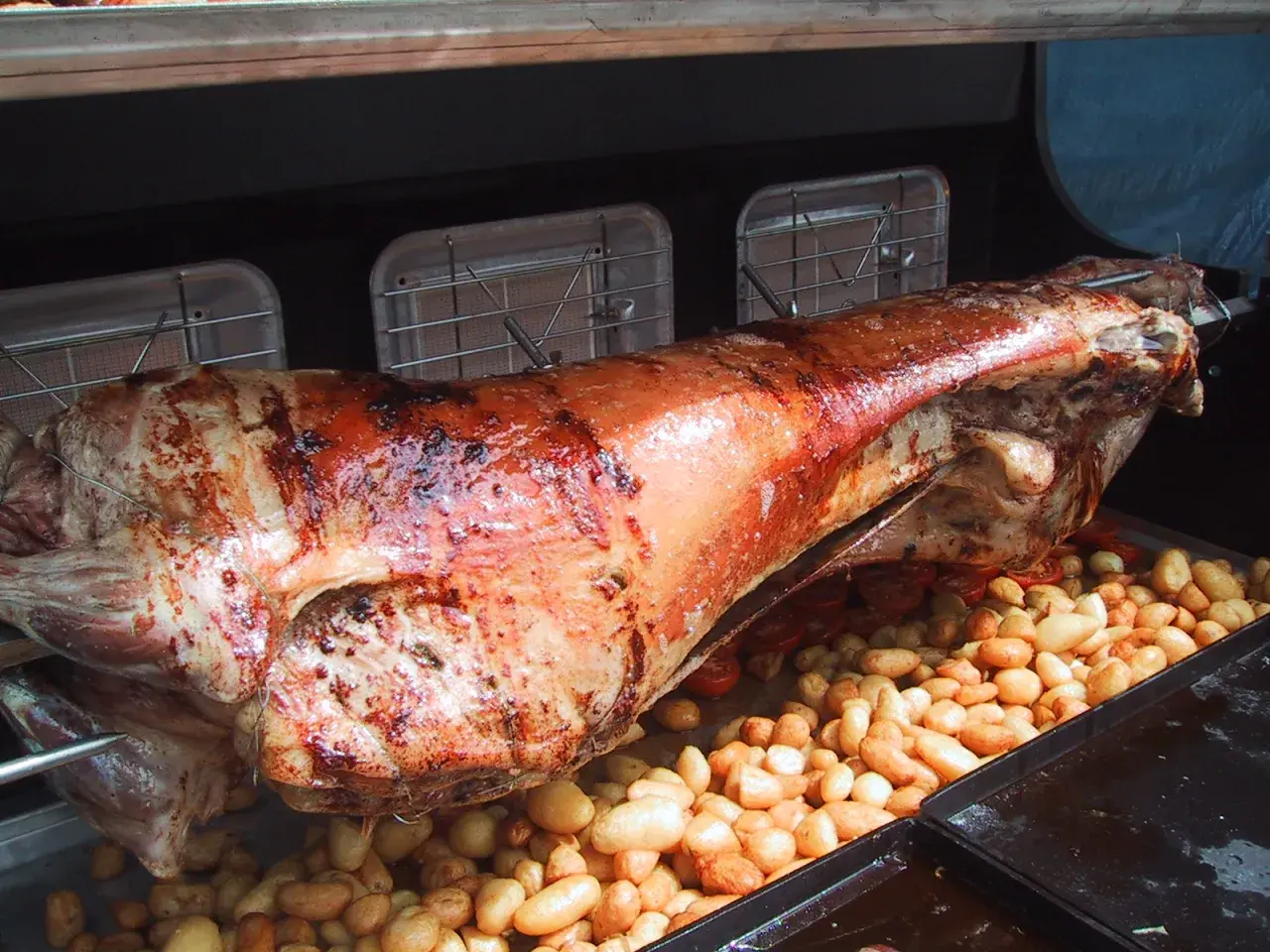 Gigot à la broche doré et juteux, rôti lentement avec des pommes de terre et des tomates cerises en dessous.
