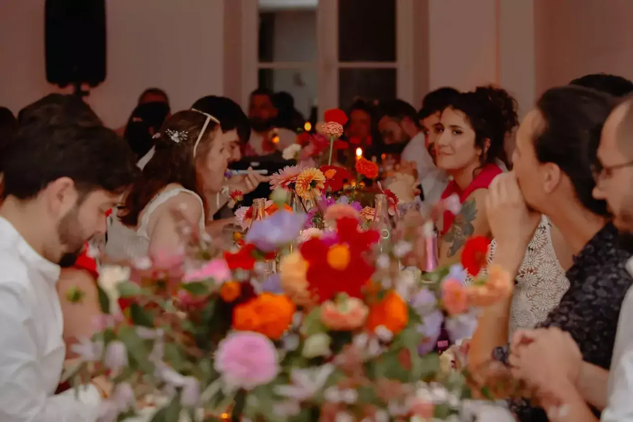 Des invités souriants partagent un repas de mariage festif, entourés de fleurs colorées. La durée du repas semble agréable.
