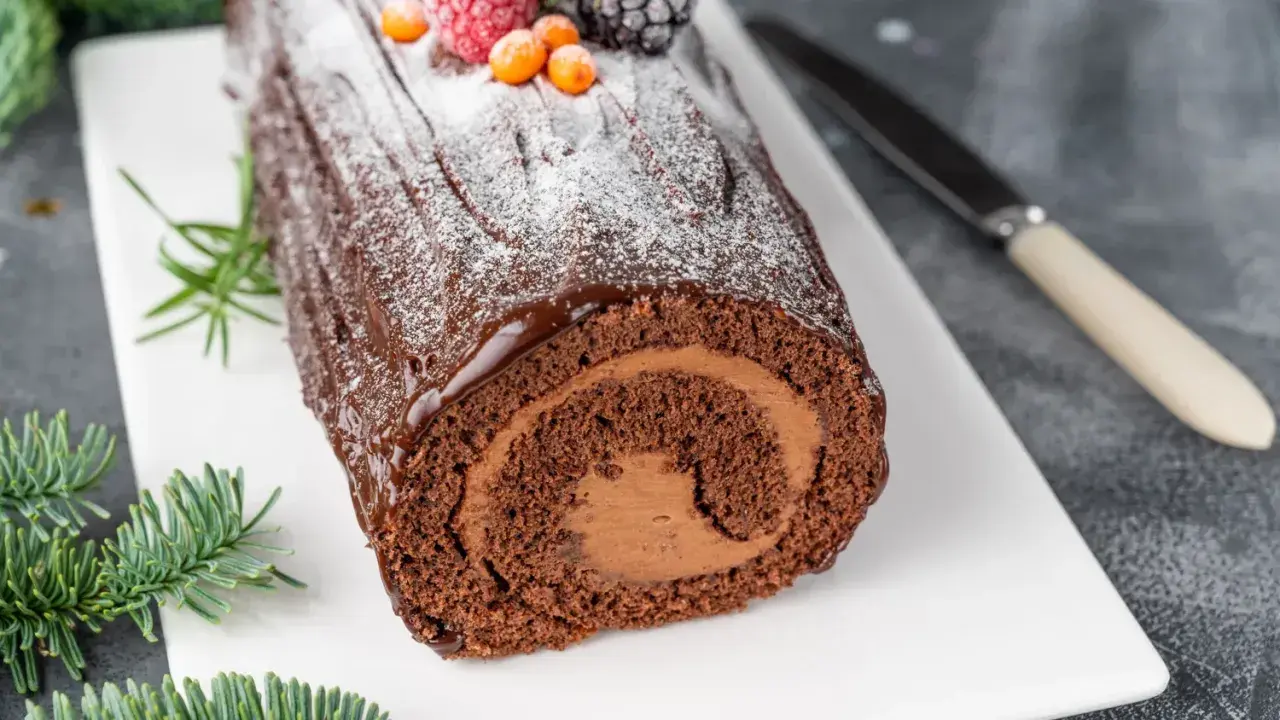 Bûche de Noël au chocolat, parfaite pour une recette génoise bûche moelleuse. Garnie de fruits rouges et de sucre glace.