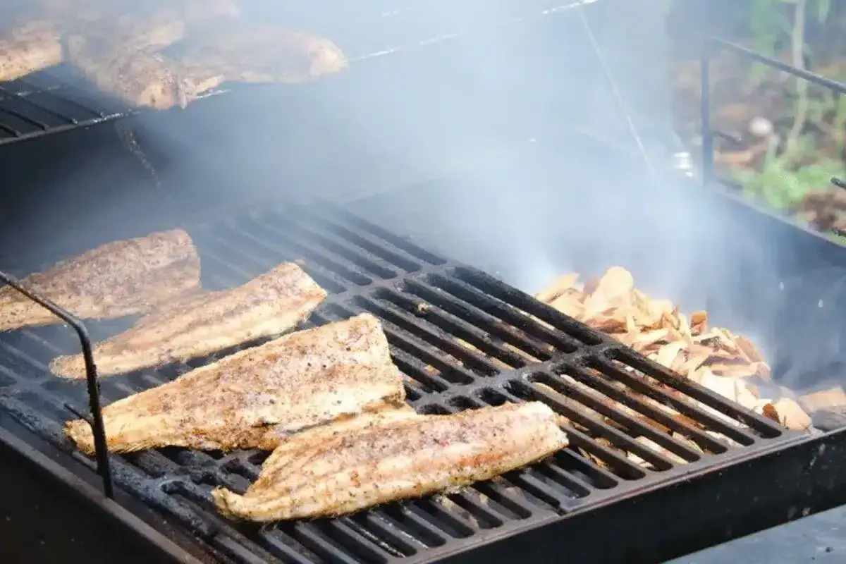 Poisson fumé sur un gril, avec des copeaux de bois qui dégagent de la fumée. Idéal pour savoir quel bois pour fabriquer un fumoir.