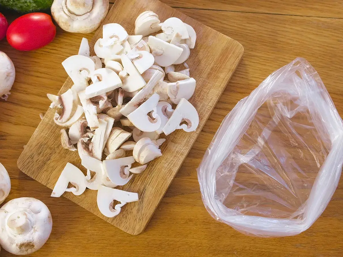 Champignons frais coupés sur une planche en bois, prêts à être mis dans un sac pour apprendre comment congeler des champignons frais.