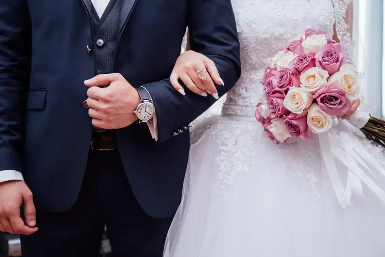Un couple uni, main dans la main, bouquet de roses roses et blanches. Vive les mariés !