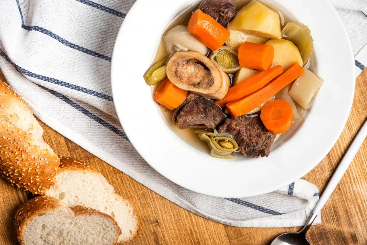 Un réconfortant pot-au-feu d'hiver avec du bœuf, des carottes, des poireaux et une os à moelle, servi avec du pain croustillant.