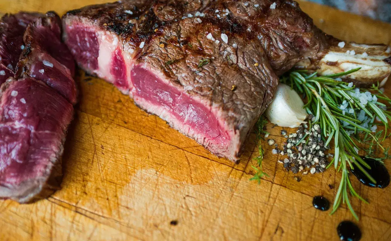Un succulent bbq côte de boeuf, saignant et parsemé de gros sel, accompagné de romarin frais et d'ail sur une planche en bois.