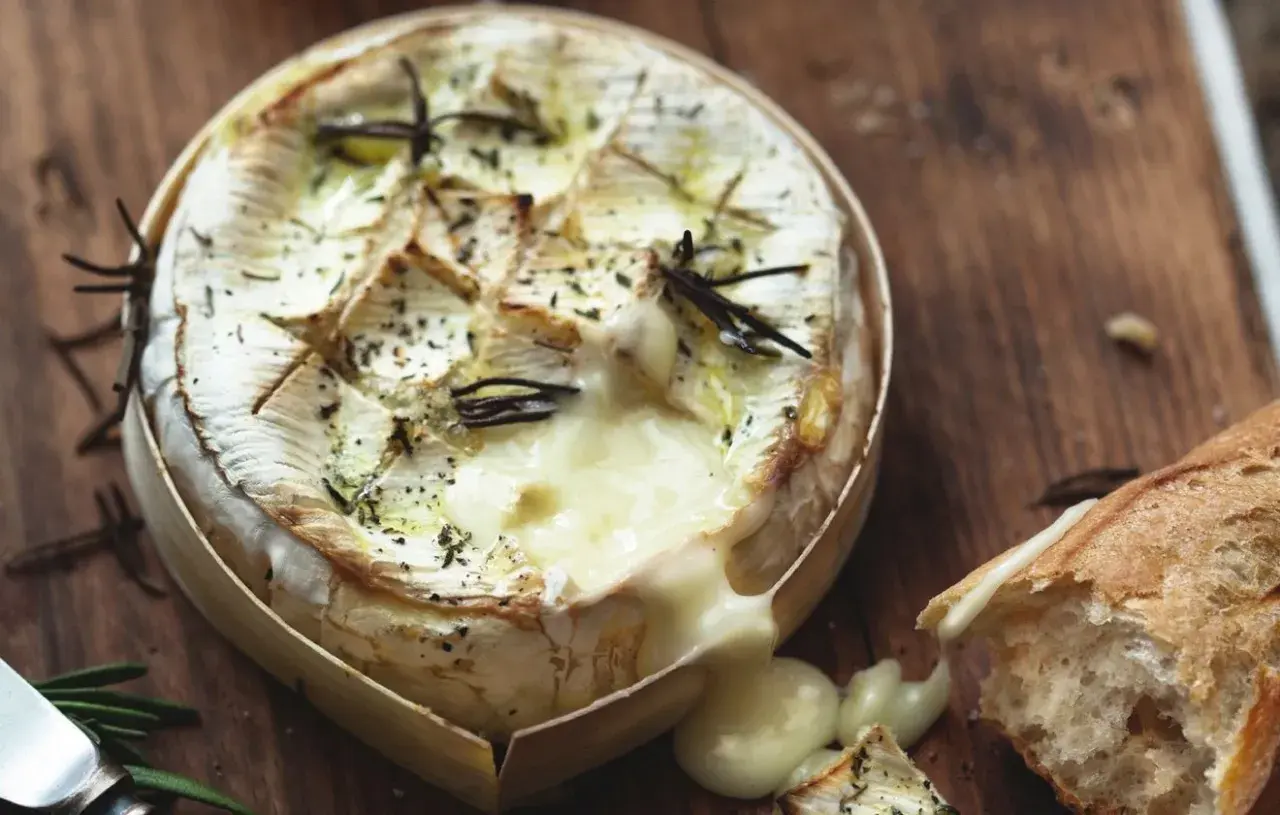 Un camembert au barbecue, fondant et parfumé au romarin, prêt à être dégusté avec une baguette croustillante.