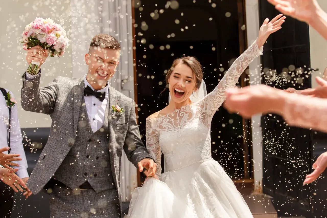 Jeune mariée et marié joyeux sortant de l'église sous une pluie de riz. Idées de mariage pour 20 personnes : une sortie mémorable !