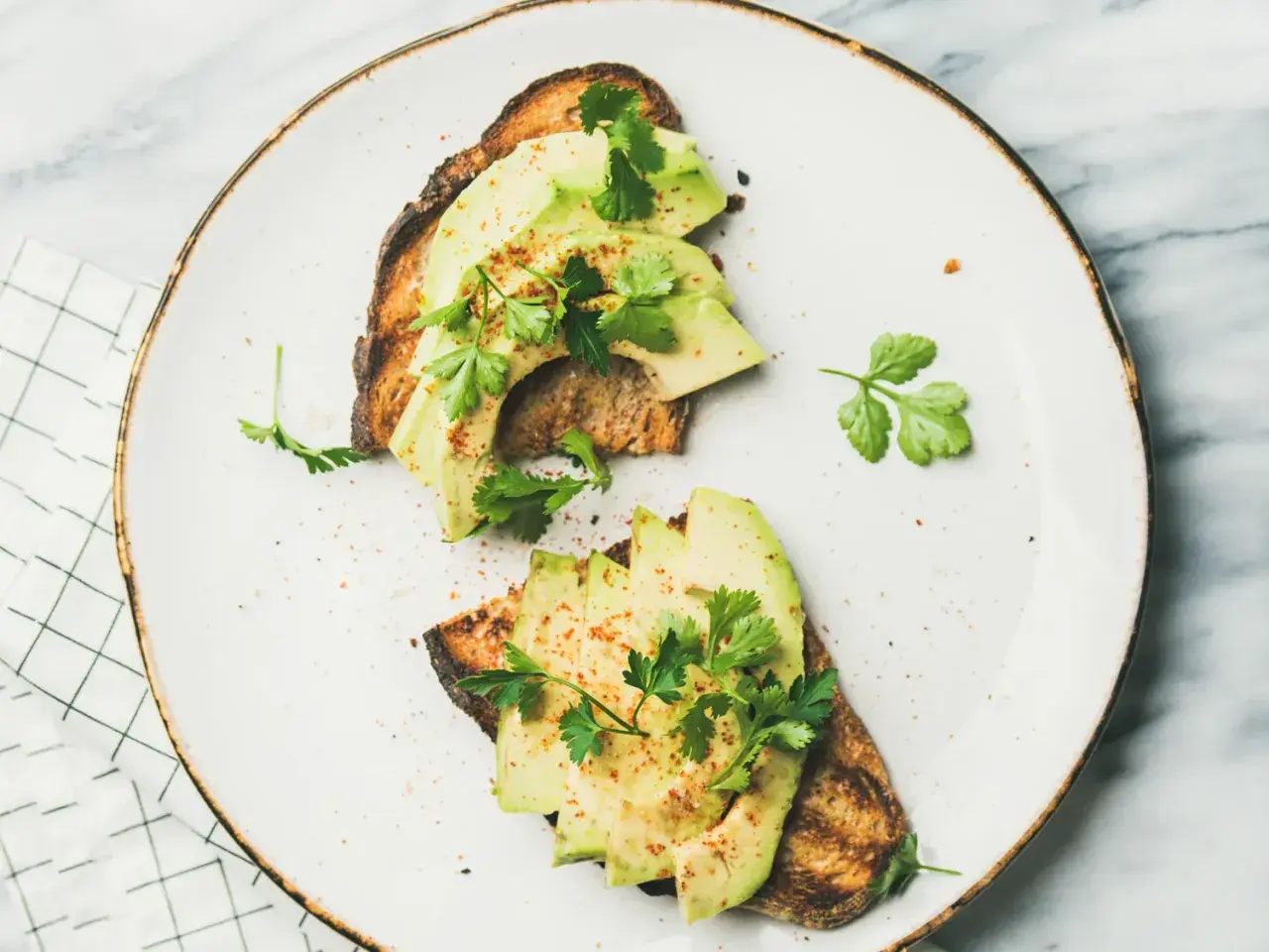 Deux toasts de pain grillé garnis de tranches d'avocat frais, parsemés d'épices et de persil. Une recette avocat simple et savoureuse.