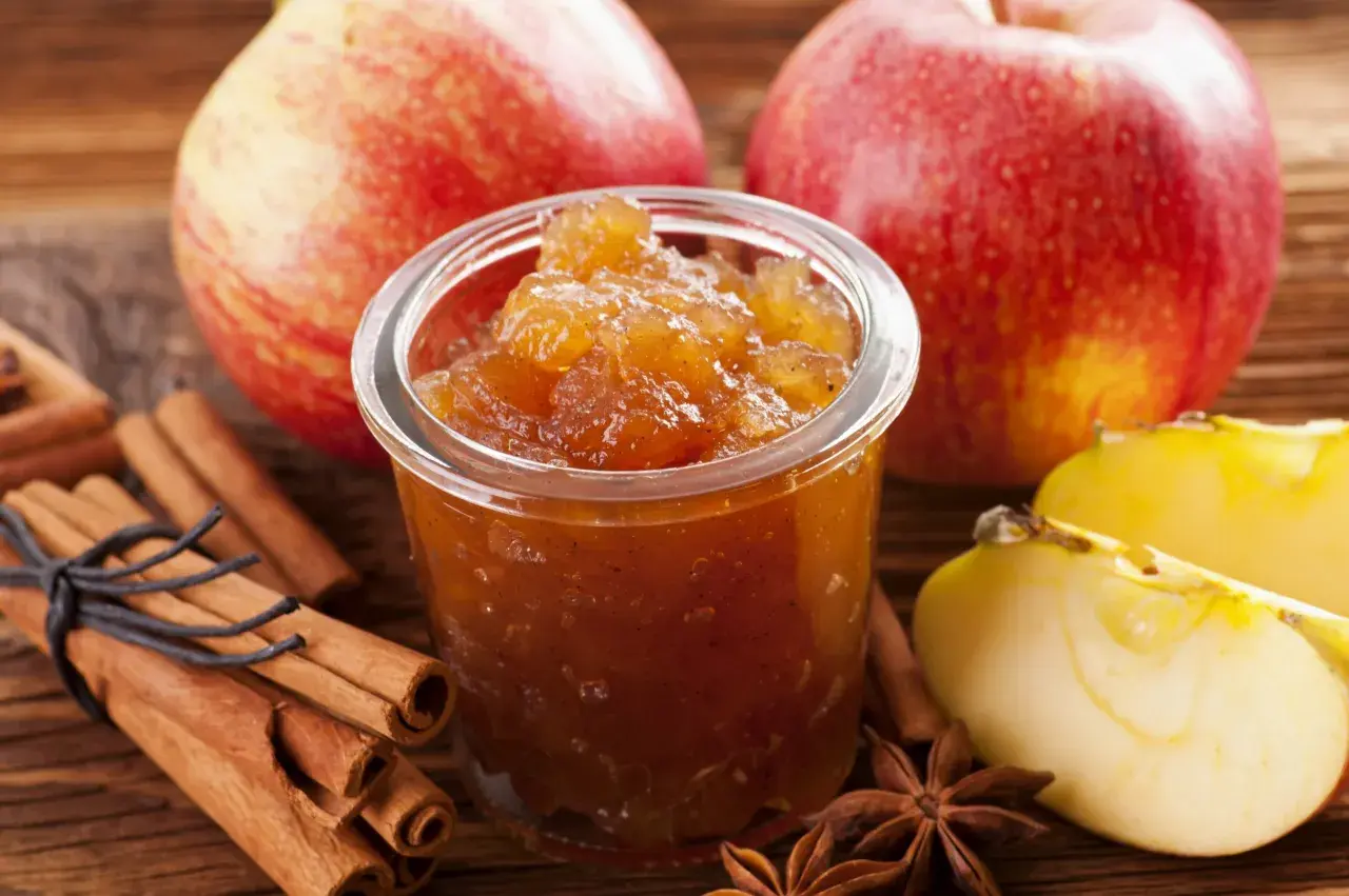 Un pot de confiture de pommes originales, avec des bâtons de cannelle, des étoiles de badiane et des pommes fraîches.