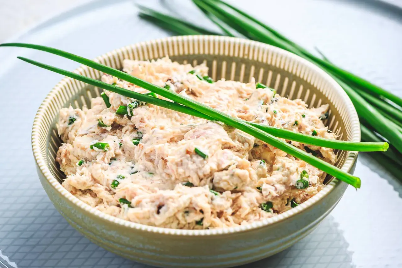 Un bol de rillettes de thon à la crème fraîche, garni de ciboule fraîche. Un délice crémeux et savoureux.