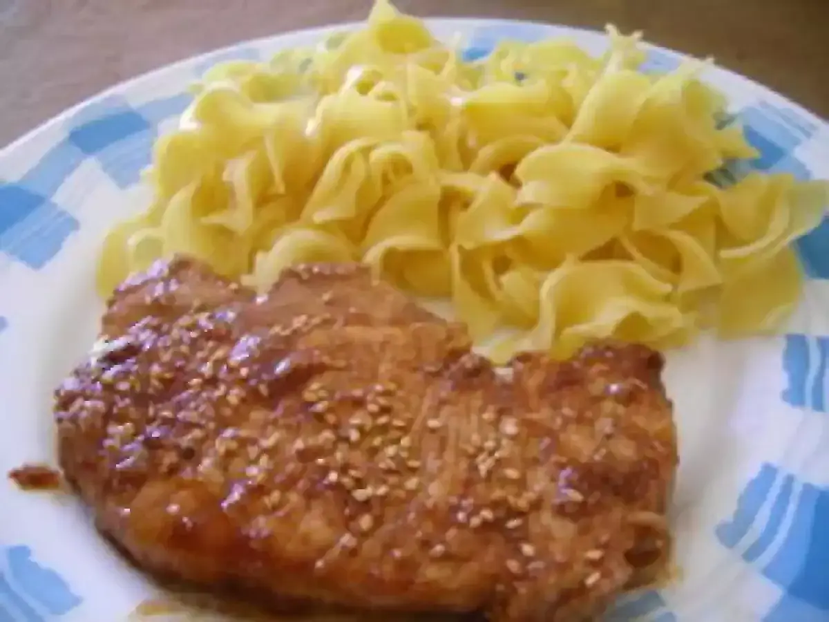 Une côte de porc savoureuse, nappée d'une sauce soja brillante et parsemée de graines de sésame, accompagnée de pâtes fraîches.