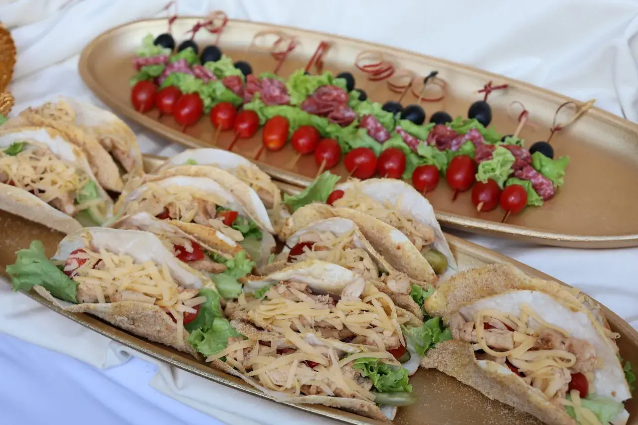 Un buffet froid mariage avec des tacos garnis de poulet, salade et fromage râpé, et des brochettes de tomates, olives et salami.
