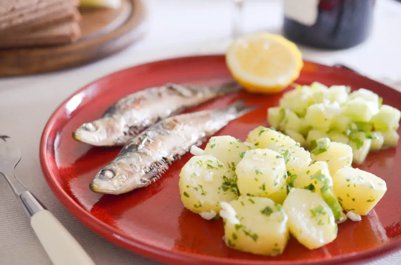 Deux sardines grillées sur une assiette rouge avec une salade de pommes de terre et de concombre. Quel accompagnement avec des sardines grillées !