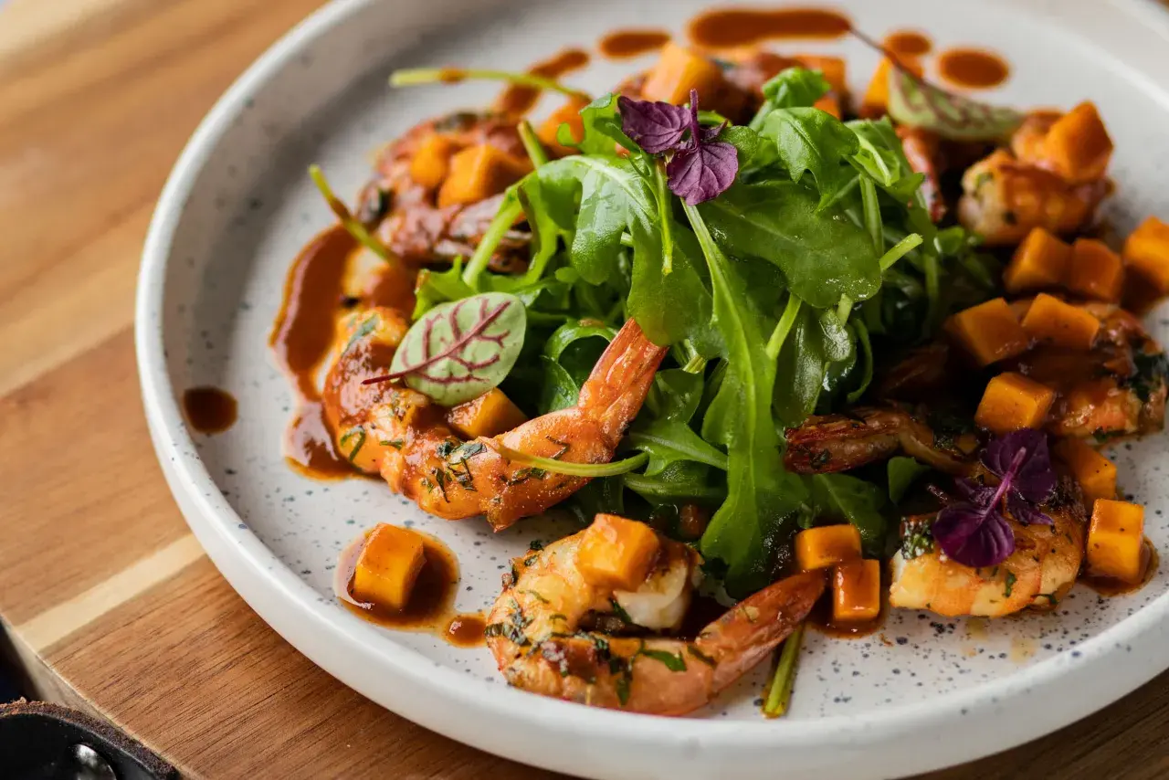Assiette de crevettes flambées, cubes de mangue et roquette, arrosée d'une sauce caramélisée.