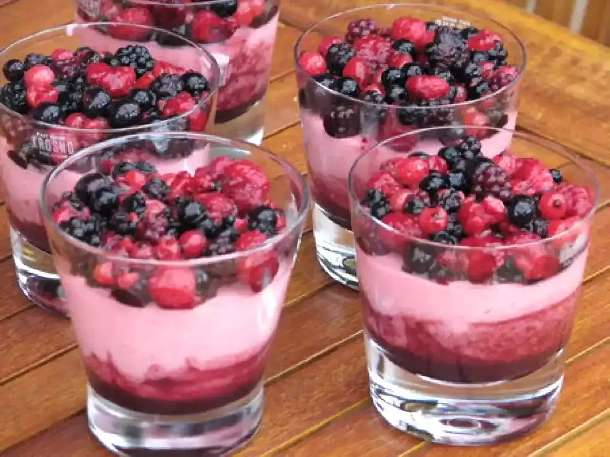 Plusieurs verrines de **dessert léger aux fruits rouges surgelés**, garnies de baies fraîches et d'une mousse rose.