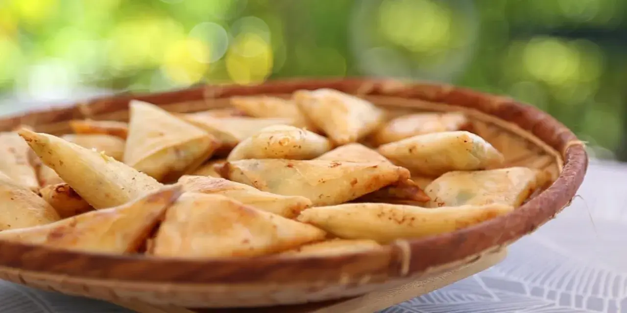 Un panier rempli de samoussas dorés, garniture pomme de terre fromage. Parfait pour un apéritif gourmand en extérieur.