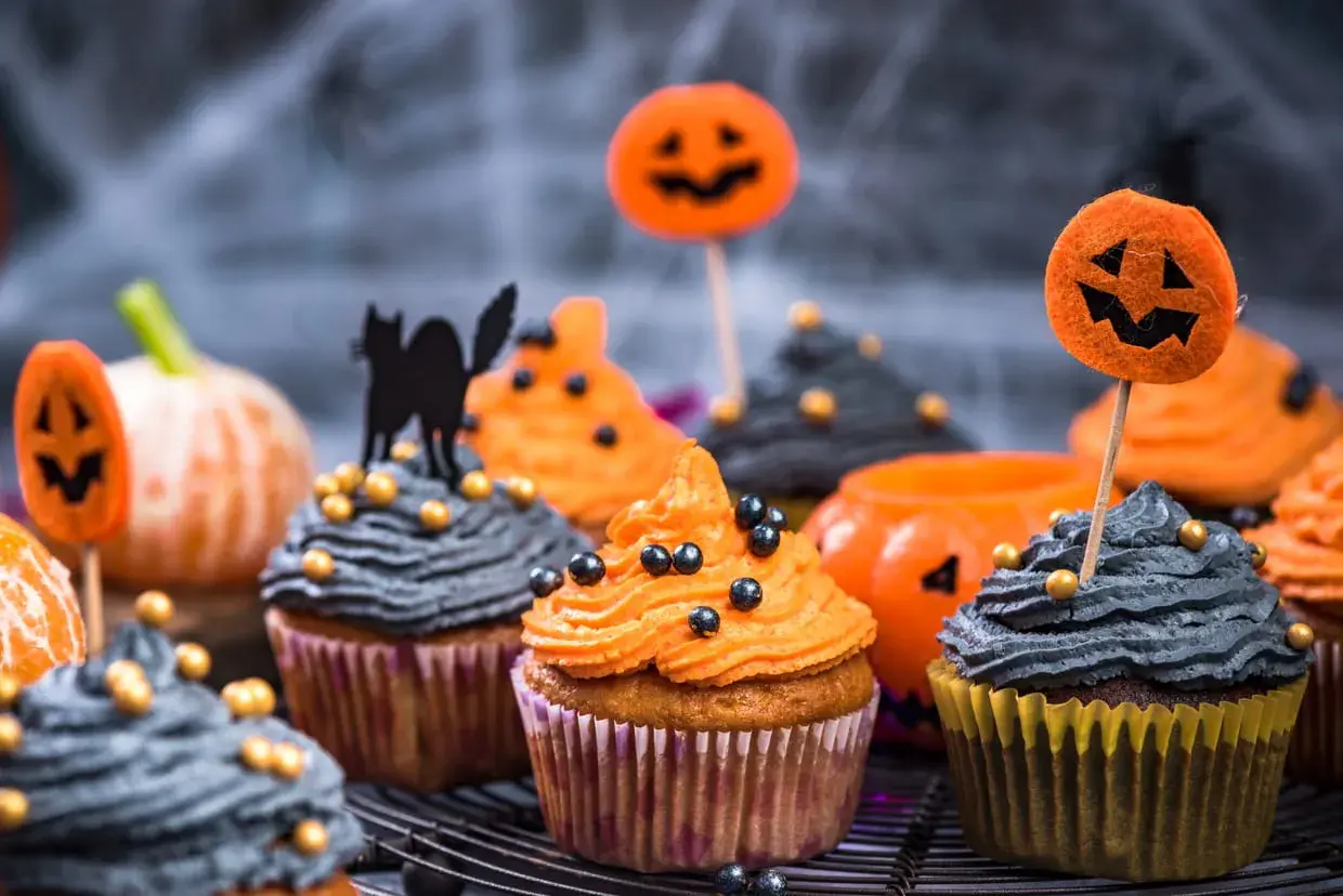 Des muffins d'Halloween effrayants, parfaits pour une recette facile. Glaçage orange et gris, décorés de citrouilles et d'un chat noir.