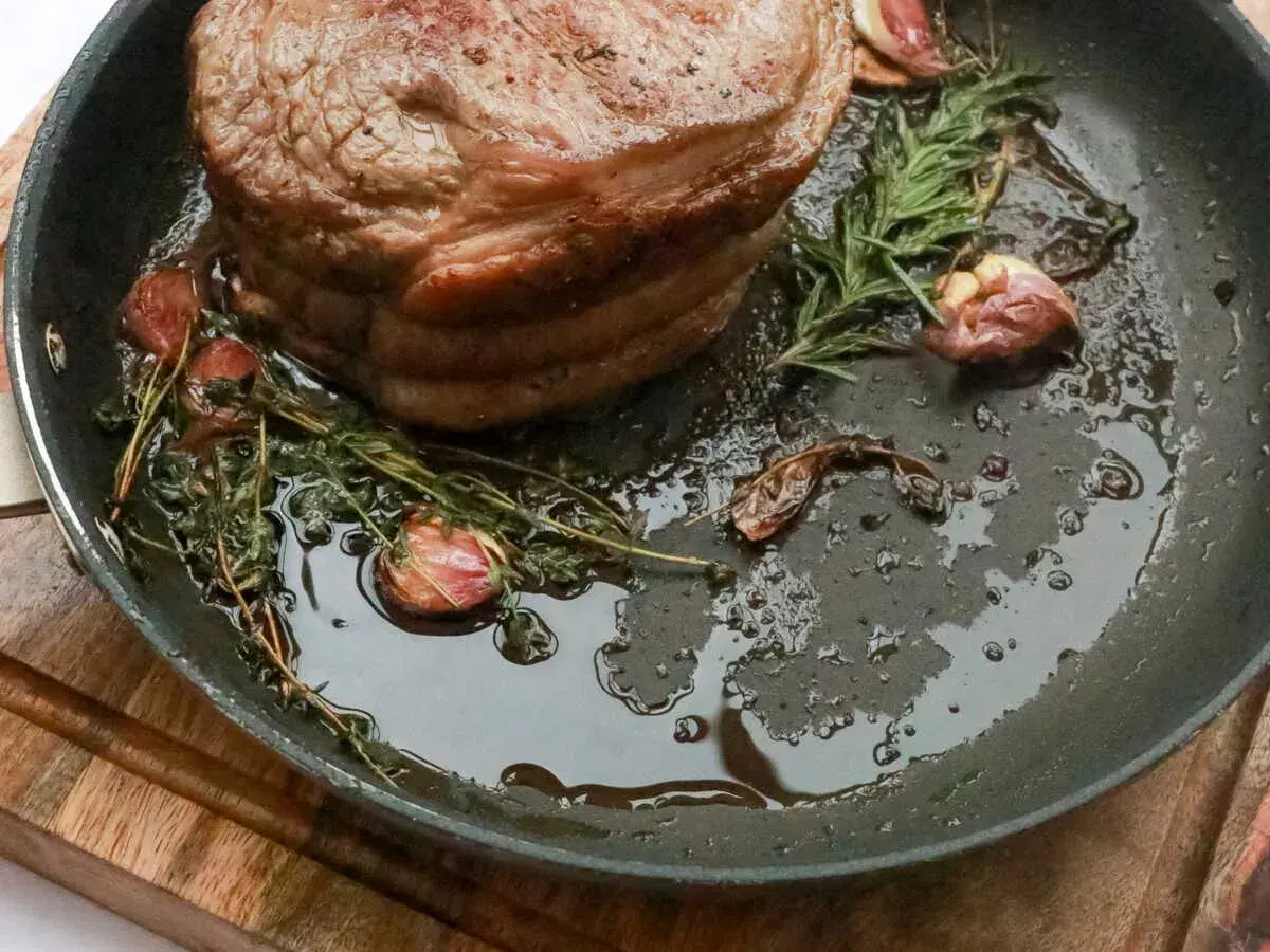 Rouelle de porc au barbecue, dorée et juteuse, mijotant dans une poêle avec de l'ail et des herbes aromatiques.