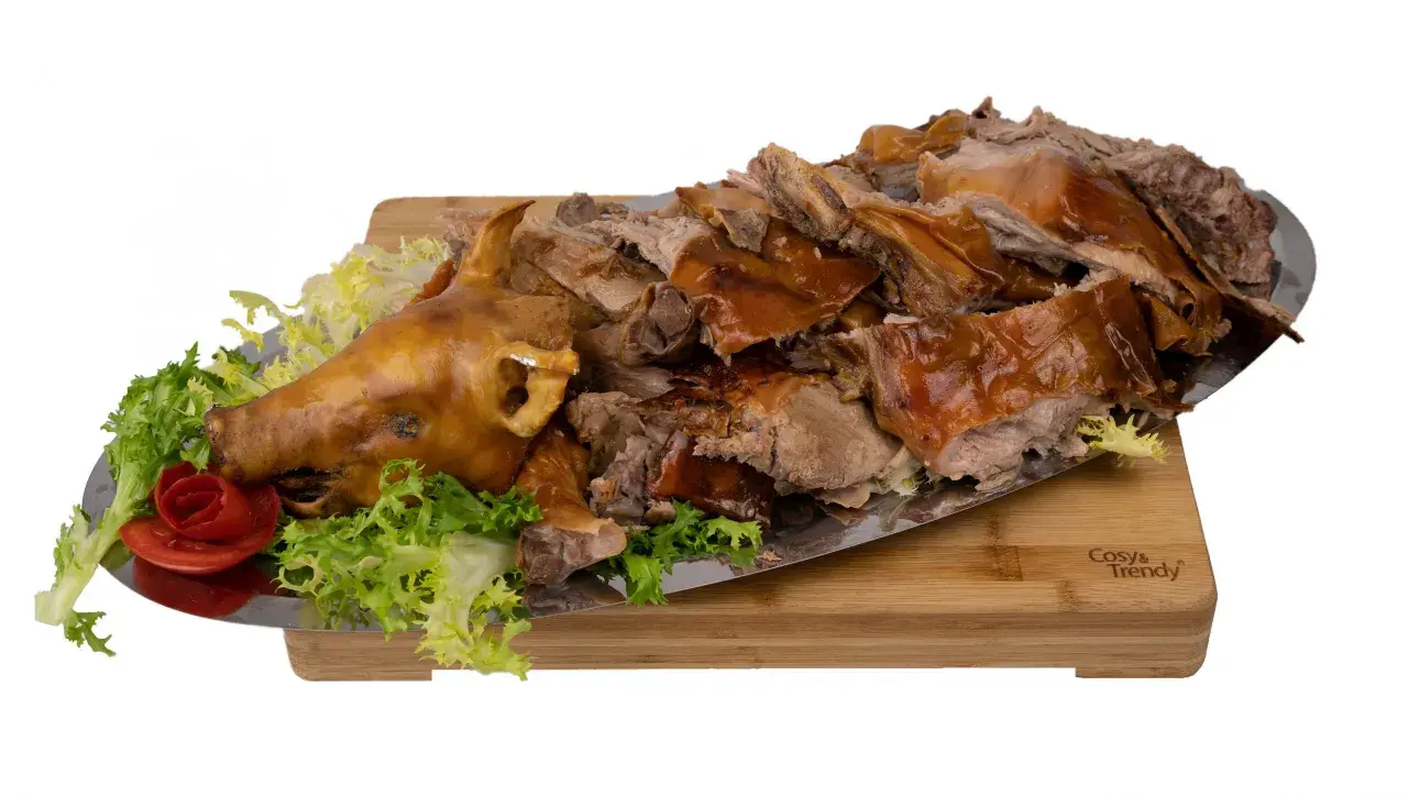 Un cochon de lait entier, rôti à la perfection, est servi sur un plateau avec de la laitue et une rose en tomate. La cuisson du cochon de lait est impressionnante.