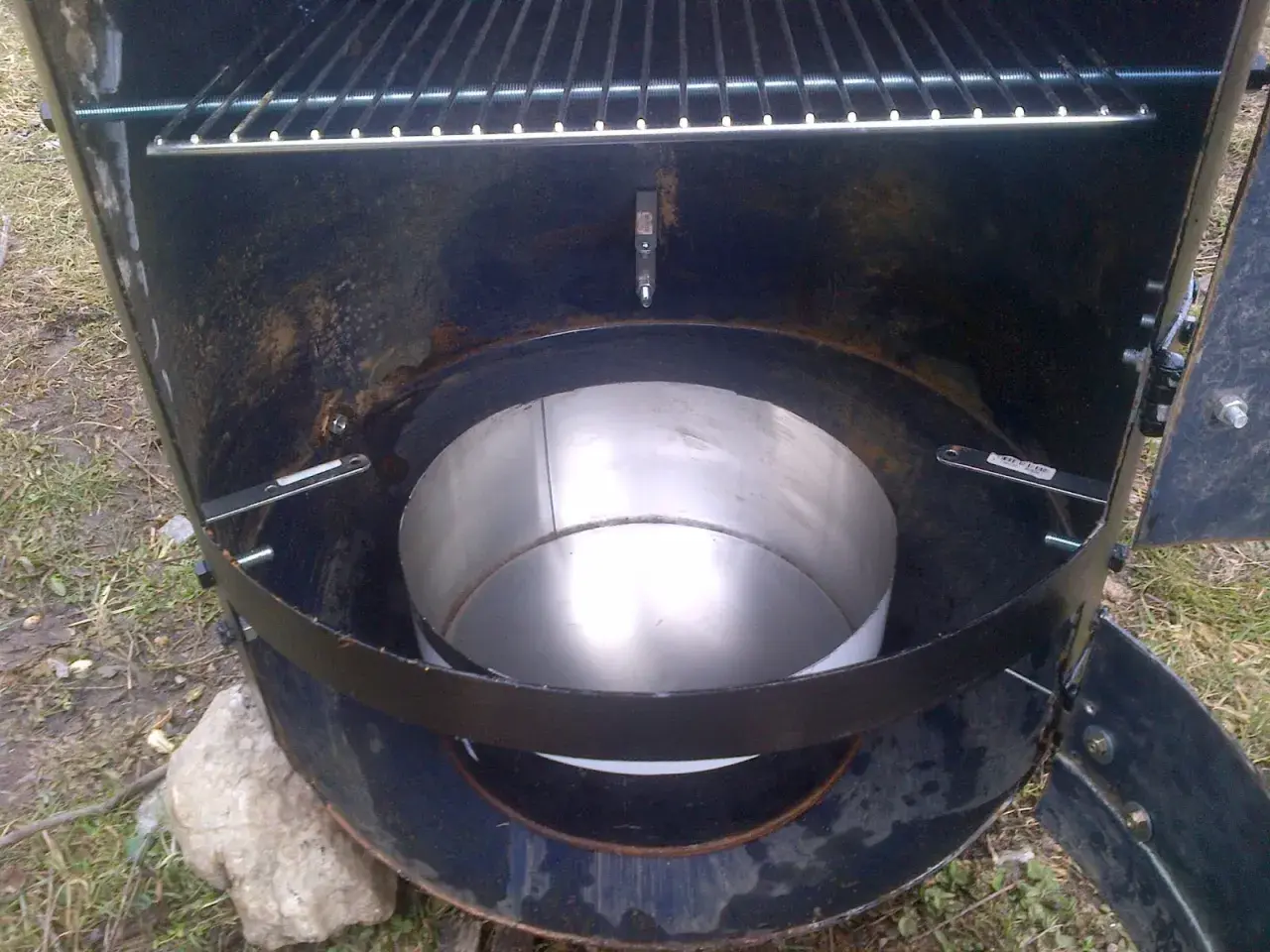 Intérieur d'un fumoir fait maison avec un bidon. Une grille est visible en haut, et un récipient métallique au centre.