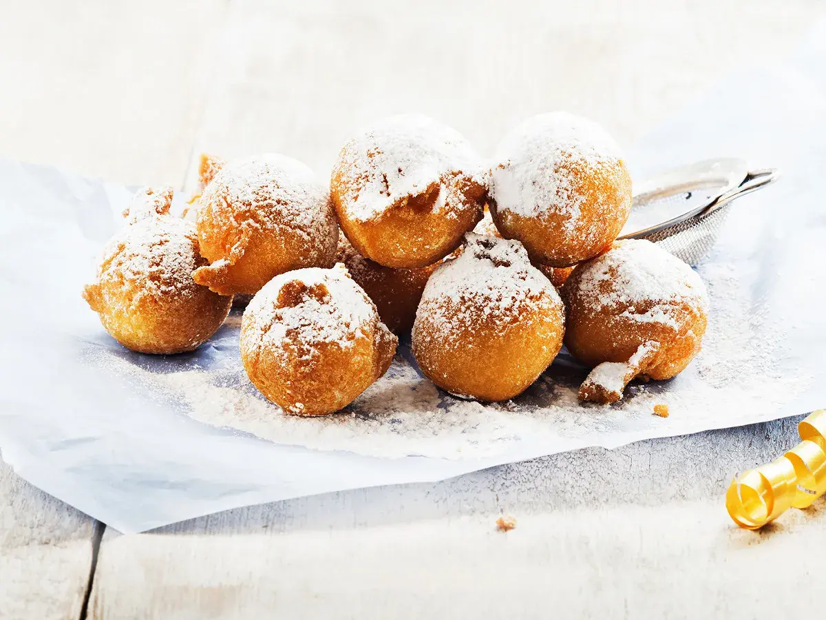 Des beignets dorés saupoudrés de sucre glace, ressemblant à des crottes d'âne, sur du papier bleu.