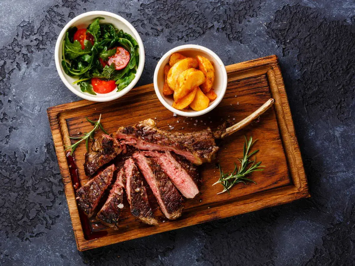 Un succulent accompagnement de côte de bœuf, servi avec une salade fraîche et des pommes de terre rôties sur une planche en bois.