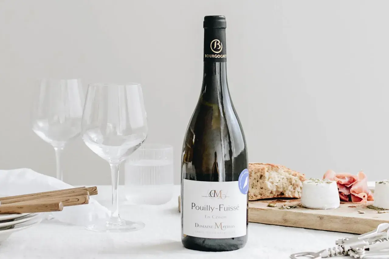Bouteille de Pouilly-Fuissé, deux verres à vin, pain, fromage de chèvre et jambon. Parfait pour une liste boisson mariage.