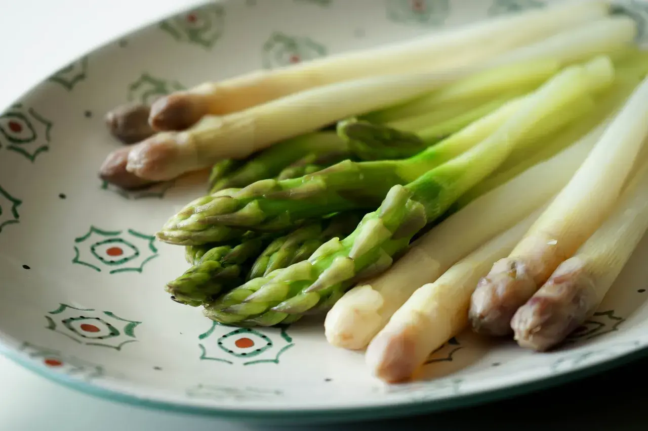 Asperges vertes et blanches sur une assiette décorée, prêtes pour la cuisson.
