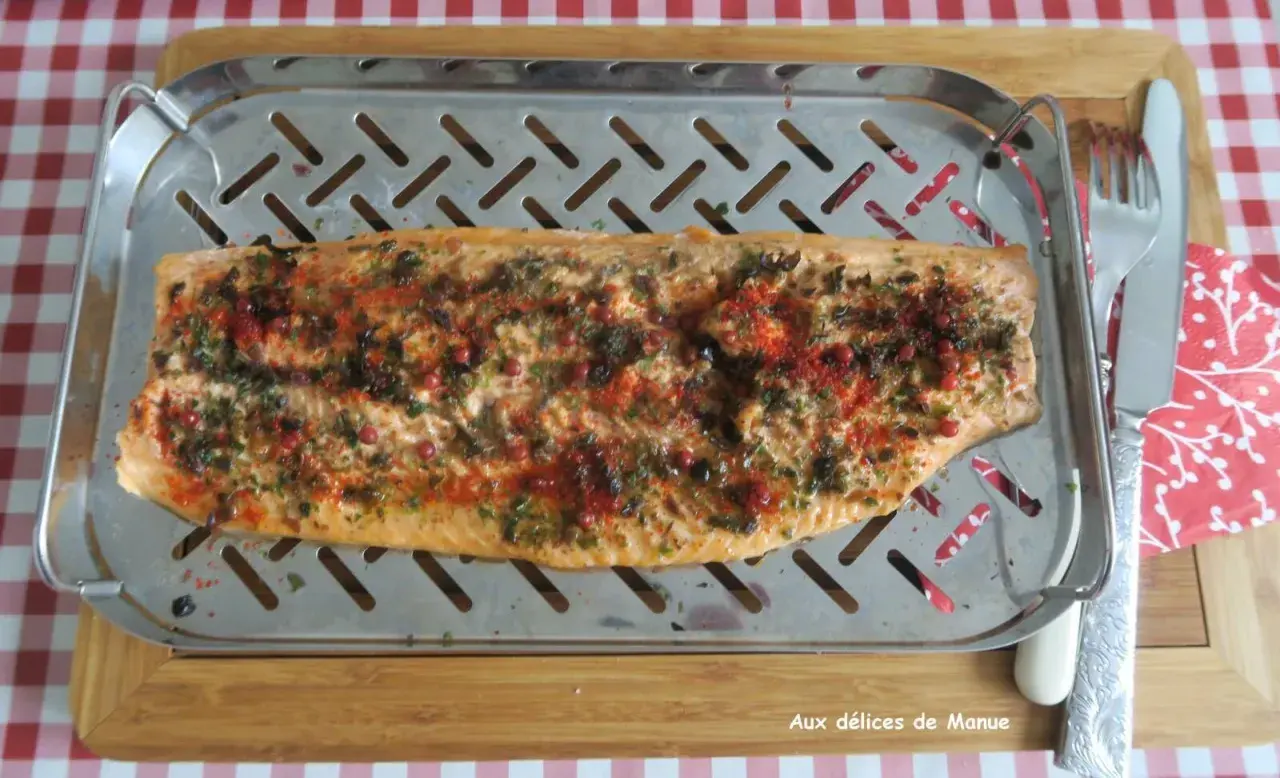 Filet de truite au four, parsemé d'herbes et de baies roses, prêt à être dégusté.