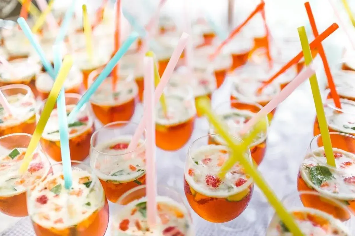 Des verres remplis de cocktails orange vif, garni de fruits et de menthe, avec des pailles colorées. Un parfait cocktail de bienvenue mariage.