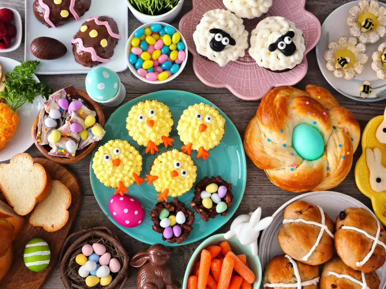 Table garnie de douceurs pascales : cupcakes moutons, poulets, biscuits abeilles, pains tressés, chocolats et bonbons. Parfaites recettes rigolotes pour Pâques !