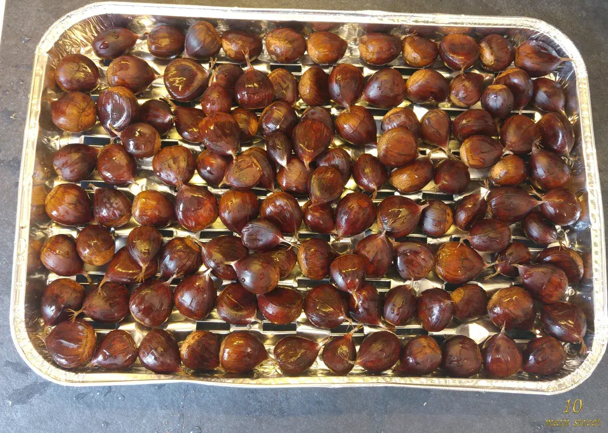 Plateau rempli de châtaignes prêtes à être grillées au barbecue. Elles sont brillantes et bien rangées.