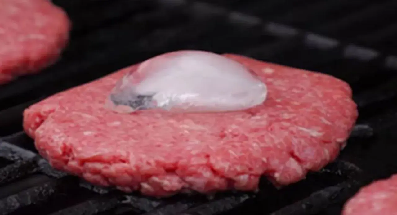 Un steak haché au barbecue, avec un glaçon posé dessus pour une cuisson parfaite.