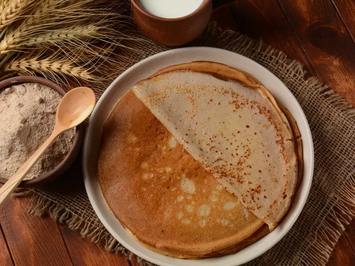 Crêpes dorées faites avec de la farine semi-complète, prêtes à être dégustées. À côté, un bol de farine et des épis de blé.