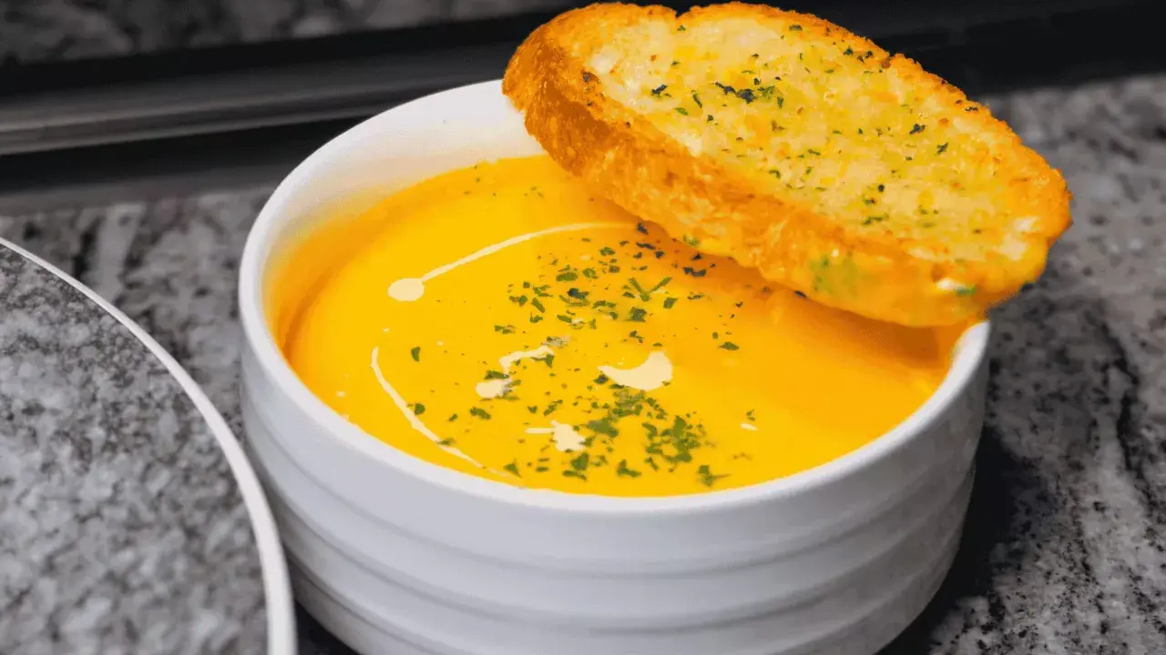 Soupe orange onctueuse, garnie d'herbes et d'un filet de crème, avec une tranche de pain à l'ail. Idéal pour savoir comment épaissir une soupe.