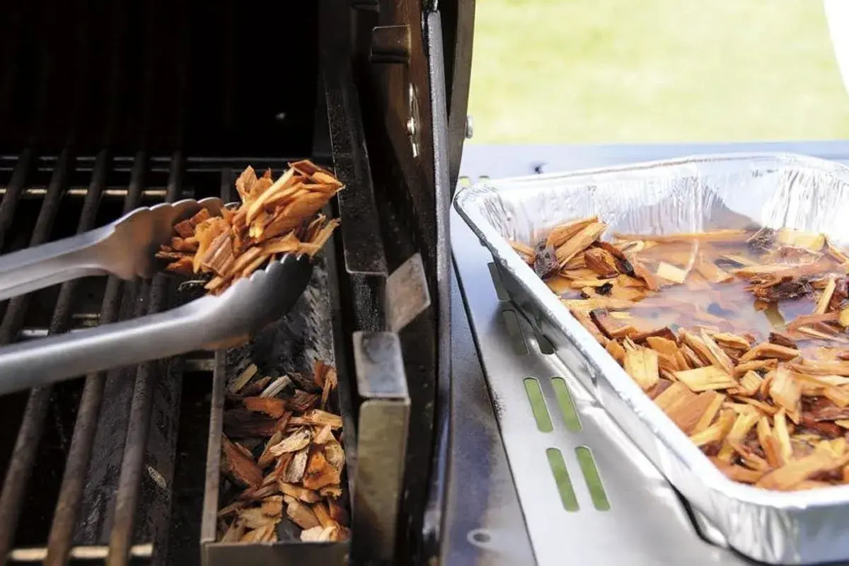 Des copeaux de bois sont placés dans un fumoir pour barbecue Weber. Une autre partie est trempée dans l'eau.