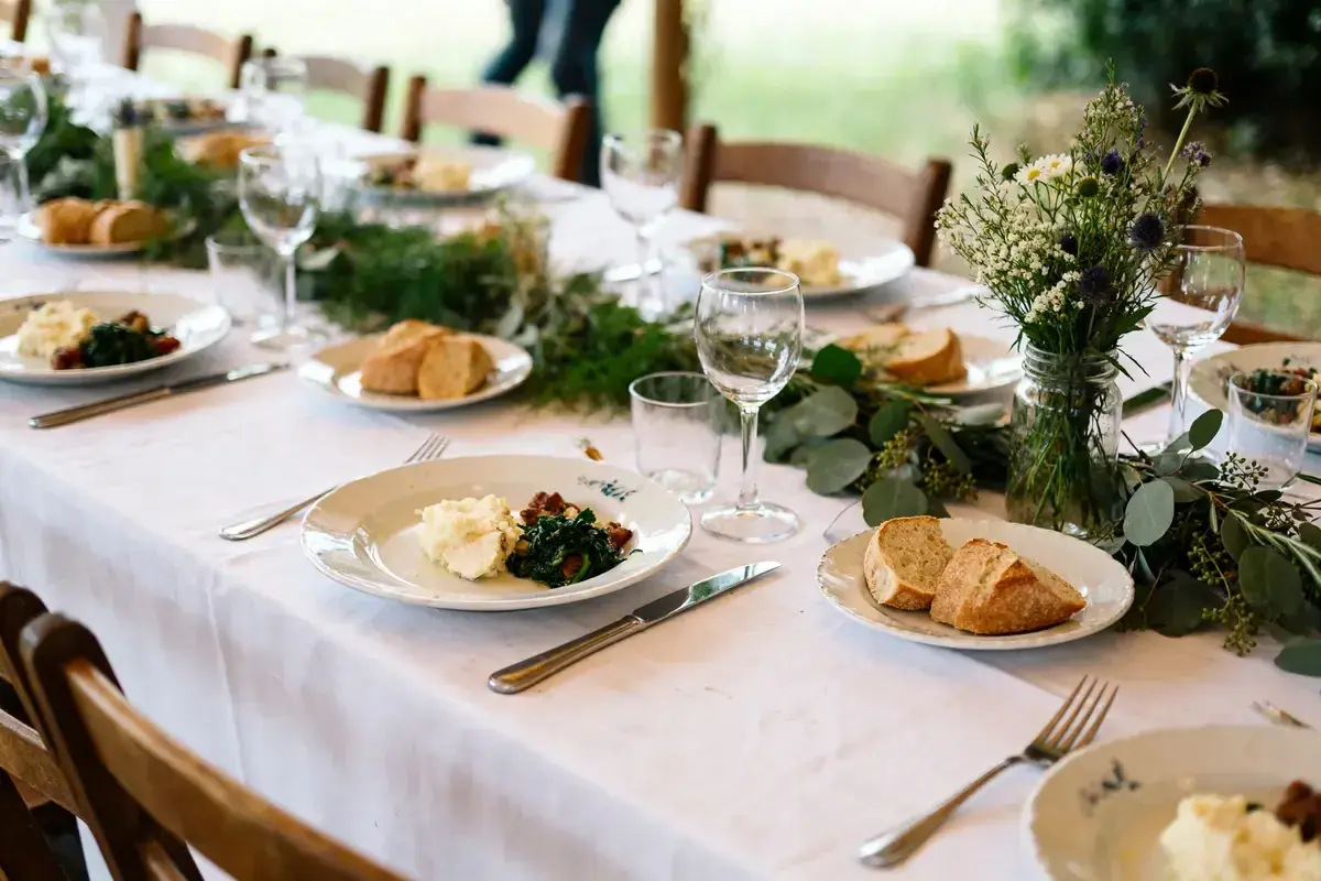 Un repas simple et champêtre, parfait pour une idée repas lendemain mariage. Des assiettes dressées avec purée, légumes verts et pain frais, entourées de verdure et de fleurs sauvages.