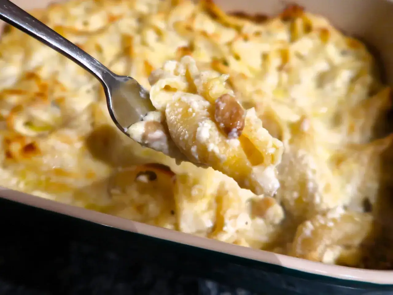 Une cuillère de conchiglioni farcis aux champignons, crémeux et dorés, sort d'un plat gratiné.