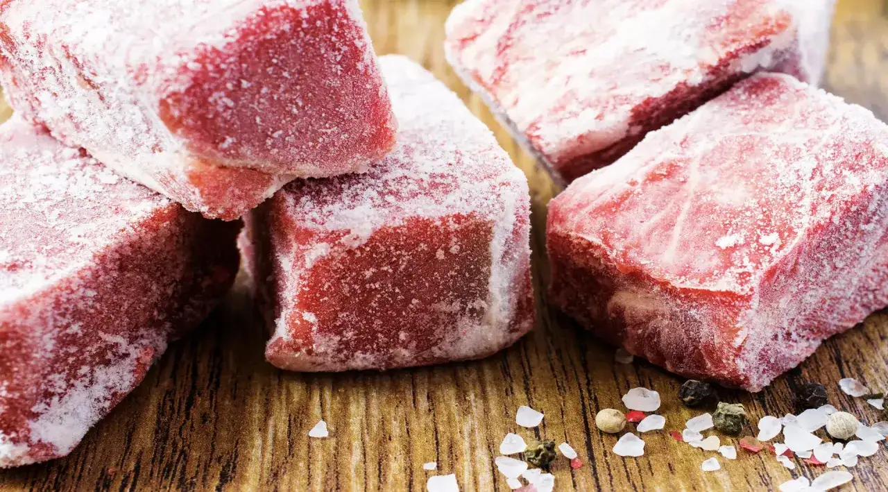 Morceaux de viande rouge givr&eacute;s, pr&ecirc;ts &agrave; d&eacute;congeler. Sel et grains de poivre sur fond de bois.