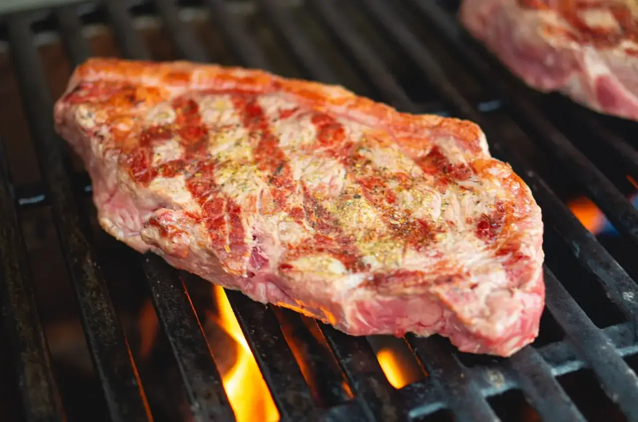 Un steak de basse côte, assaisonné et grillé au barbecue, avec des flammes vives en dessous.