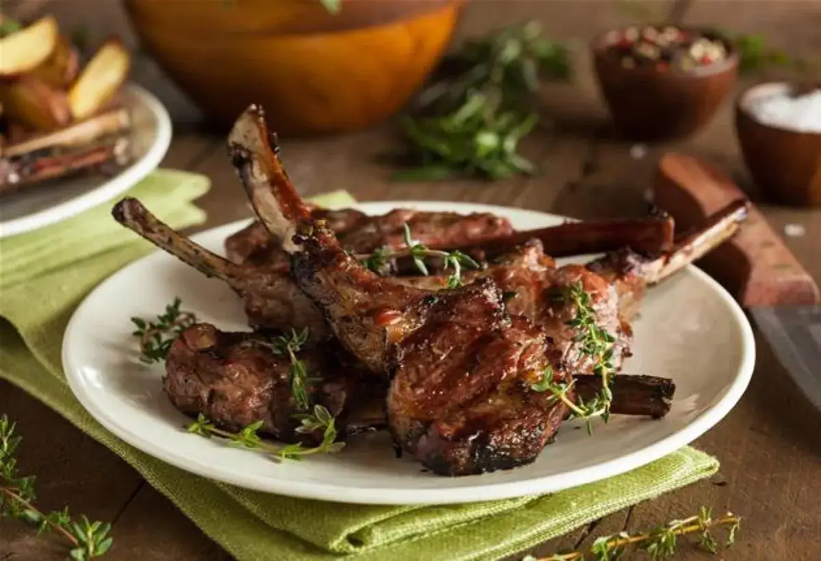Délicieuses côtes d'agneau rôties au four, garnies de thym frais, sur une assiette blanche.